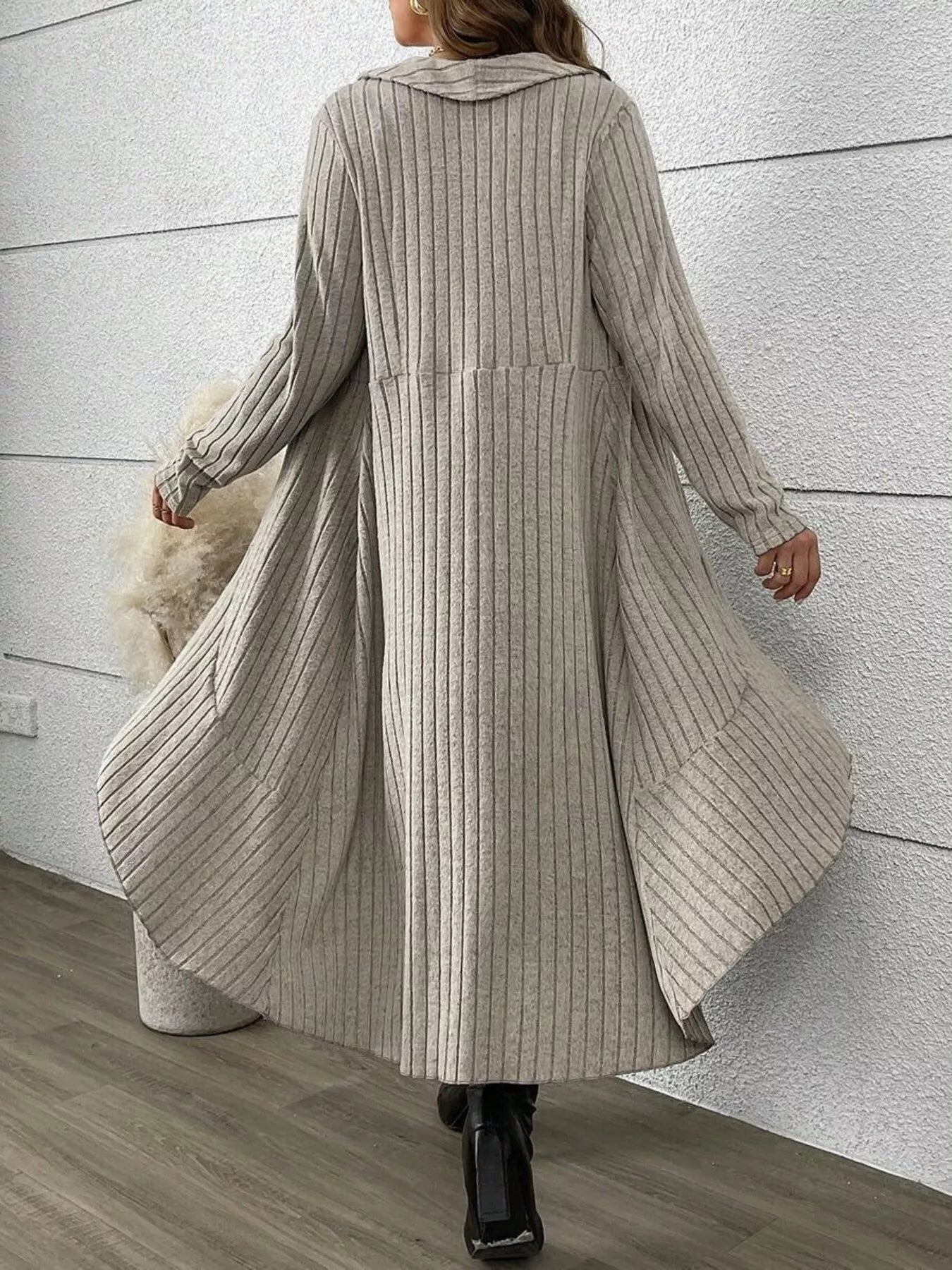 Person wearing a long ribbed knit cardigan against a light gray wall.