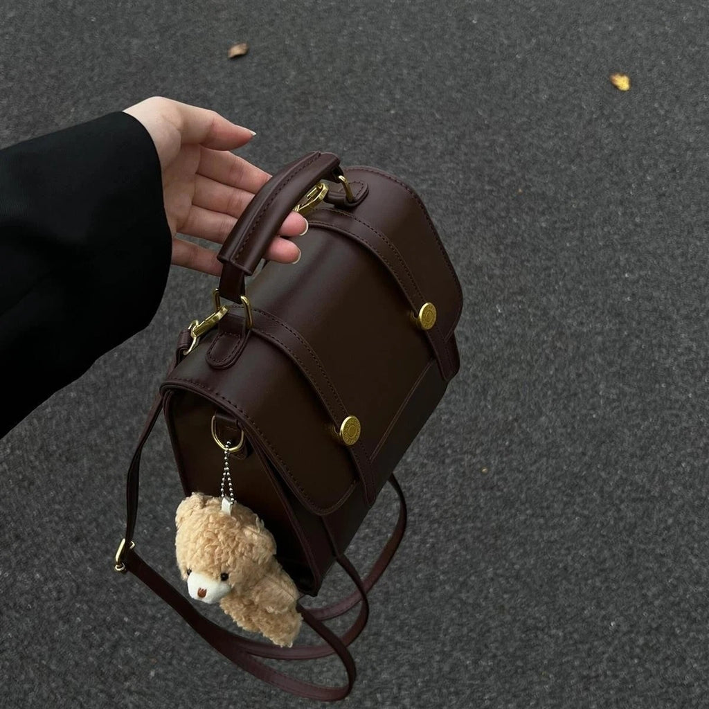 Brown leather backpack with teddy bear keychain held by a hand on a dark surface