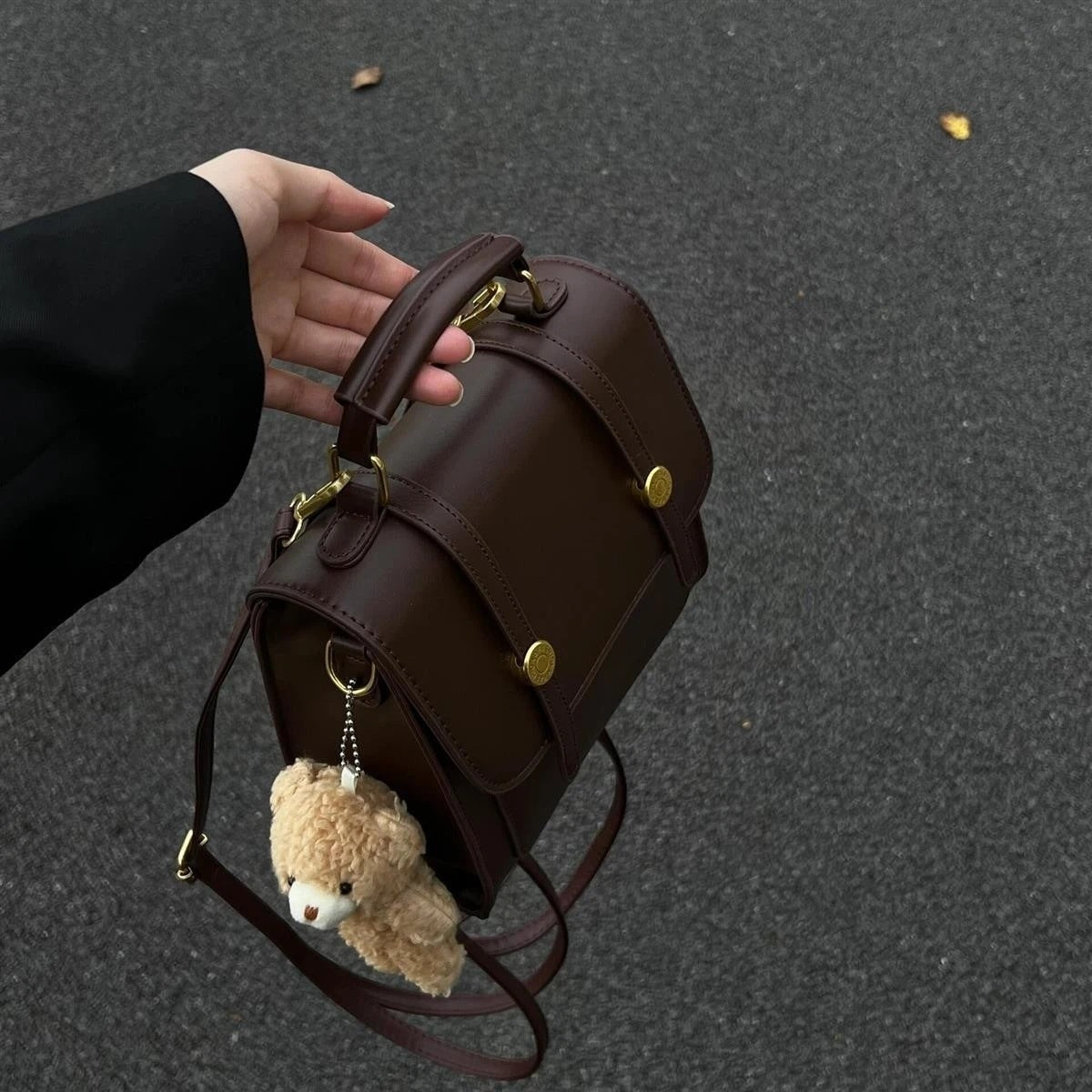 Brown leather backpack with teddy bear keychain held by a hand on a dark surface