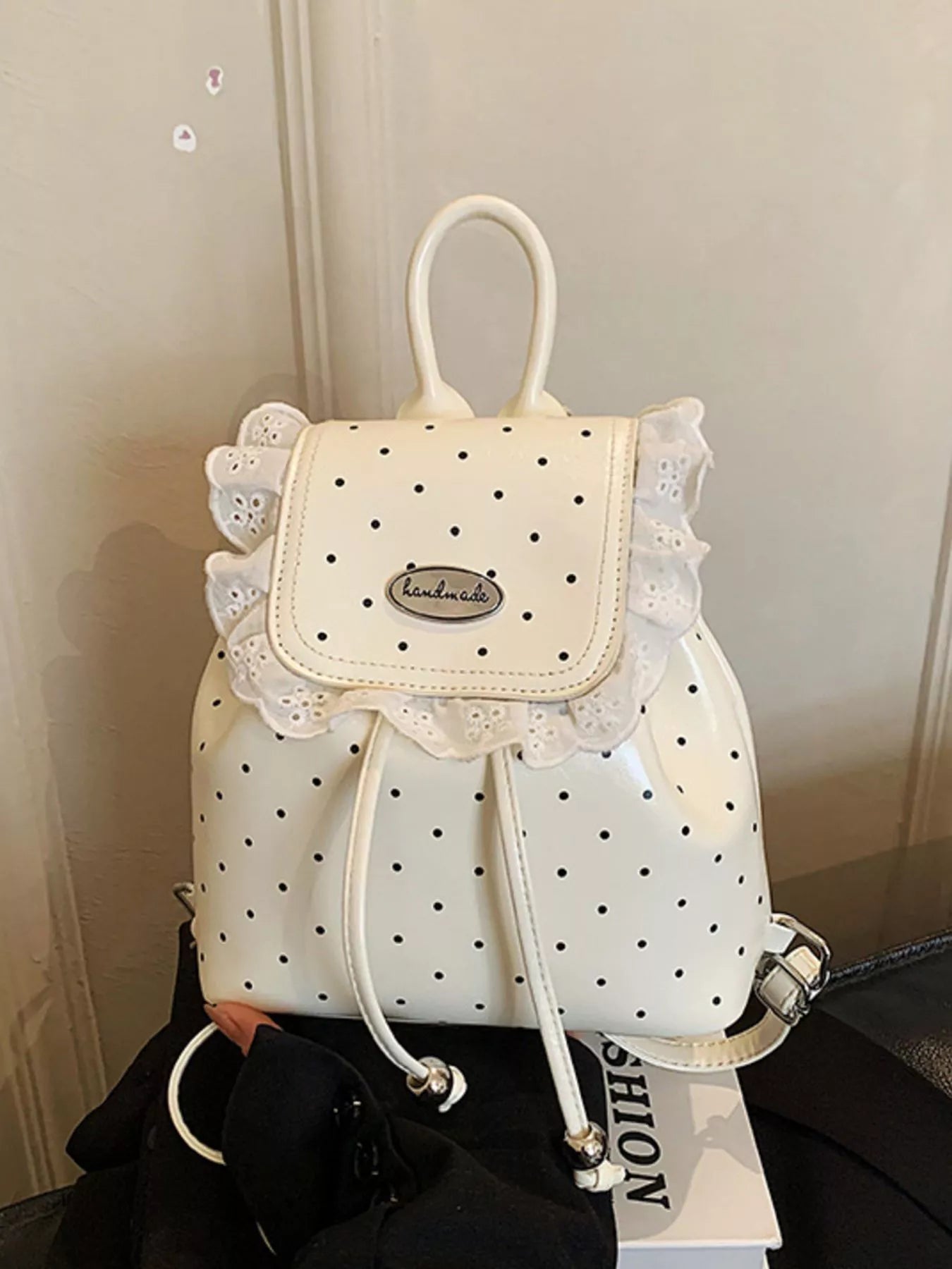 White polka dot backpack with lace details on a neutral background