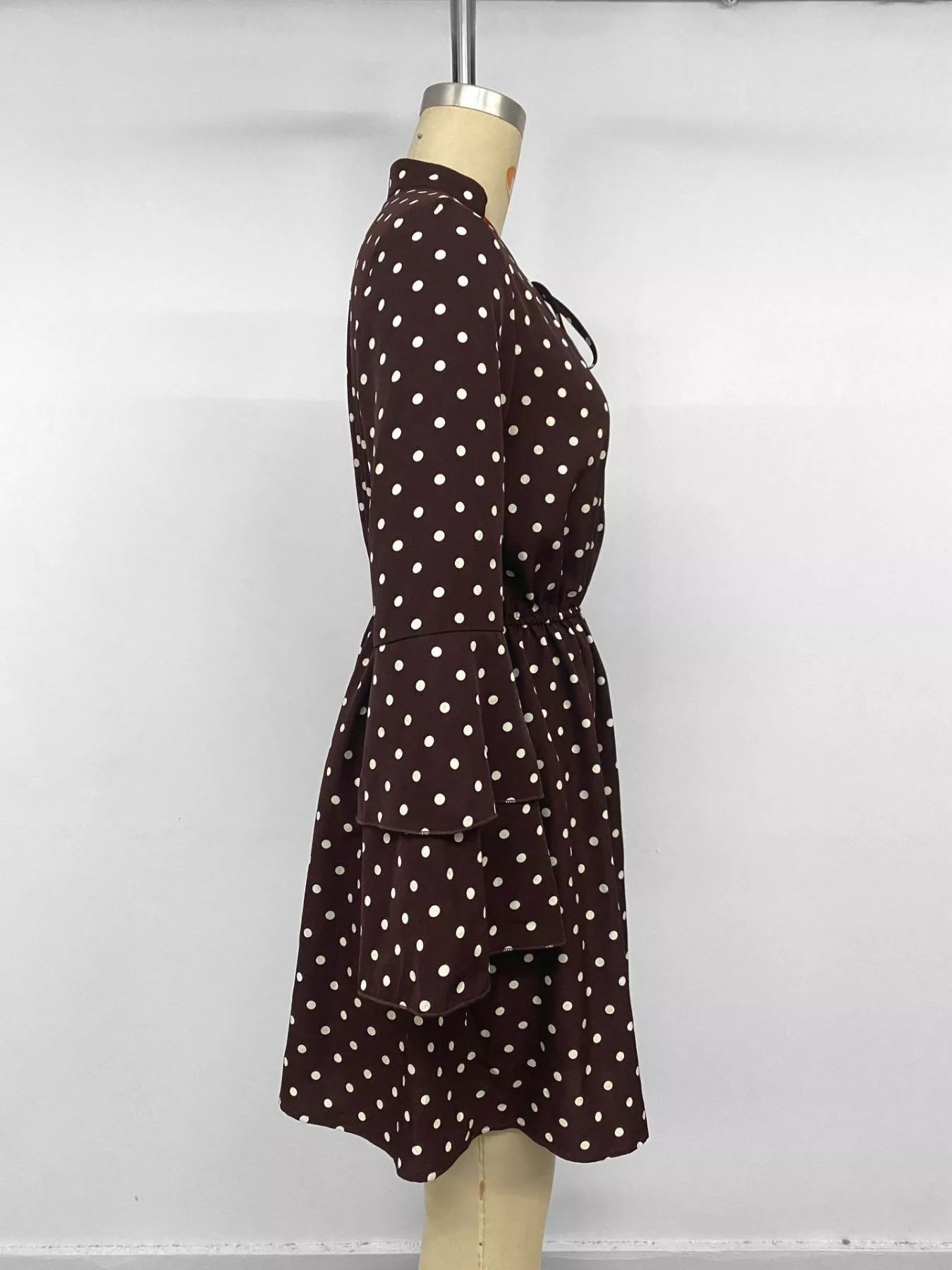 A dark brown long-sleeve dress with white polka dots, displayed on a beige dress form mannequin against a plain white background.
