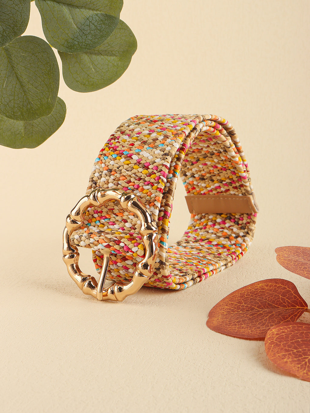 Multicolored woven belt with a gold buckle on a beige background with leaves and wood pieces.